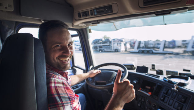 Portrait of truck driver sitting in his truck holding thumbs up. Transportation and trucking services.